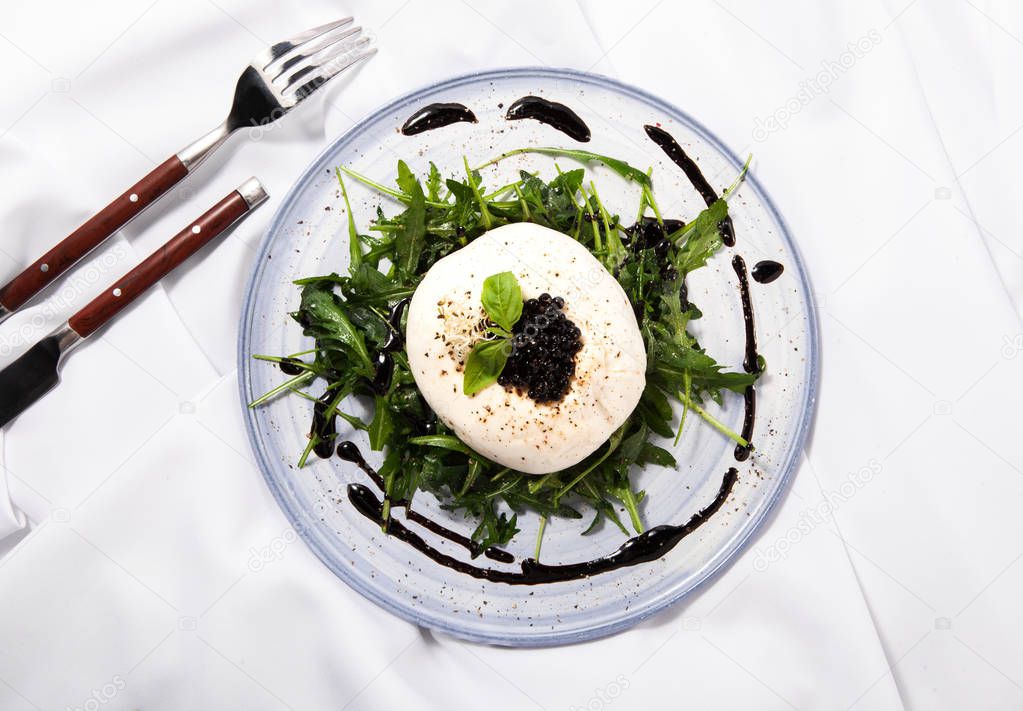 Burratta cheese with arugula and balsamic vinegar pearls on a white background