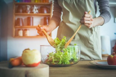 Kahvaltı, öğle ve akşam yemeği hazırlanıyor genç bir kadın elinde. O ahşaptan yapılmış, pota içinde bir salata tabağı, cam, ahşap kesme tahtası elma ile karıştırın malzemeyi kullanması.
