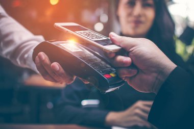 Genç adam ellerin yemeğe para için bir kredi kartı okuyucudan dosyalama bir Qr kodu taramak için Smartphone ve içecekler restoranlarda Asyalı kızlar tarafından romantik bir atmosfer var birlikte oturuyorsun.