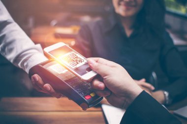 Genç adam ellerin yemeğe para için bir kredi kartı okuyucudan dosyalama bir Qr kodu taramak için Smartphone ve içecekler restoranlarda Asyalı kızlar tarafından romantik bir atmosfer var birlikte oturuyorsun.