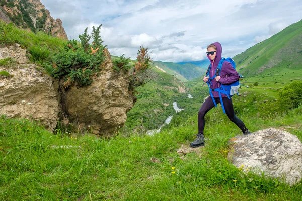 Girl with a backpack in the mountains. Trekking along the mountain road.