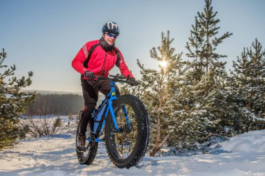 Man riding a mountain bike with big fat tires and helmet on a snow. Fat bike. clipart