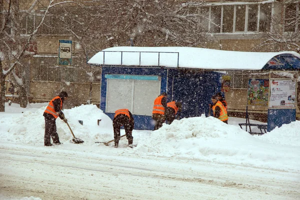 Workers clean the bus stop from snow during heavy snowfall in the city hard winter