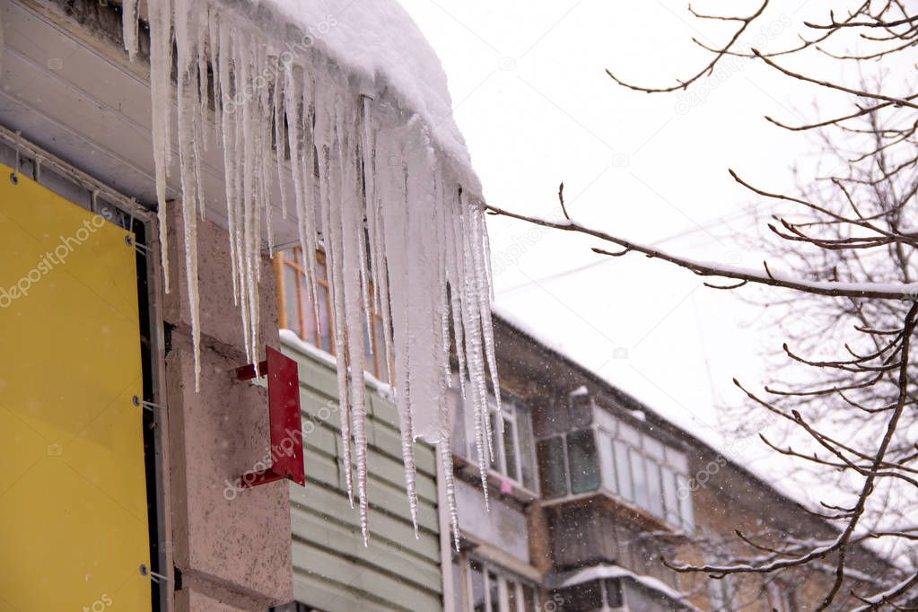 Large iced icicles hanging from the roof of the house , a danger to passersby