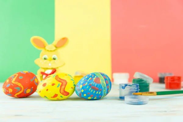 Πασχαλινά αυγά σε πολύχρωμη ξύλινη φόντο με χρώματα, βούρτσα και λαγουδάκι του Πάσχα — Φωτογραφία Αρχείου