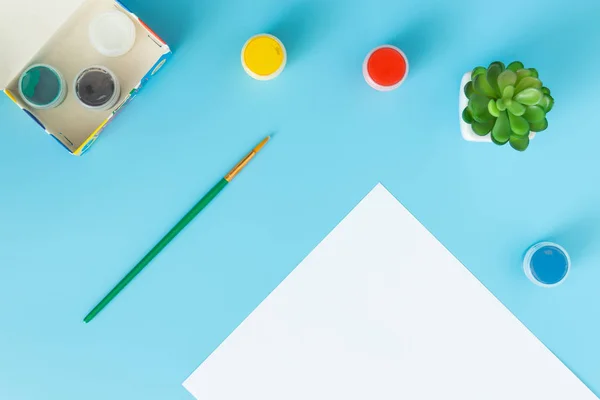 Hoja blanca de papel con pinturas verdes suculentas, multicolores y pincel sobre fondo azul con lugar para la inscripción — Foto de Stock