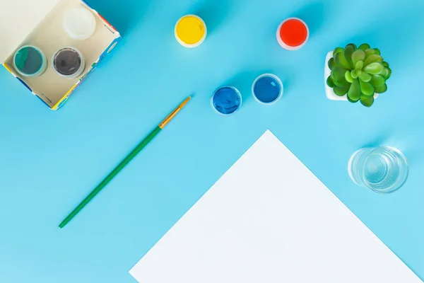 Hoja blanca de papel con pinturas verdes suculentas, multicolores y pincel sobre fondo azul con lugar para la inscripción — Foto de Stock