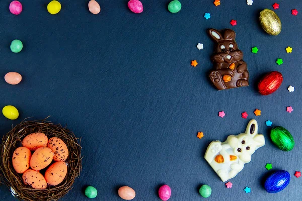 Πασχαλινά αυγά στη φωλιά, σοκολατένια αυγά και καραμέλες. Κορυφαία προβολή σε πέτρινο τραπέζι με χώρο για τις ευχές σας πολύχρωμη εικόνα — Φωτογραφία Αρχείου