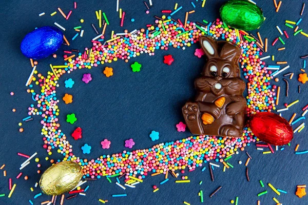 Cartão de Páscoa com moldura de doces coloridos e ovo de Páscoa, coelho de chocolate e ovos . — Fotografia de Stock