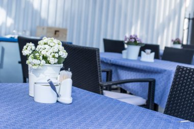 Kovada beyaz bir çiçek olan bir açık hava restoranında bir masa