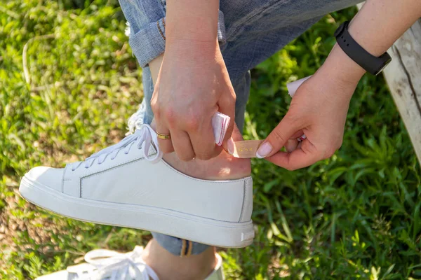 Using bactericidal medical adhesive plaster at street during wearing leather sneakers. Foot skin care and prevention of corns and calluses. First aid