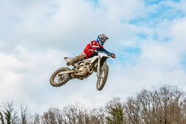 Racer op een motorfiets tijdens de vlucht, springt en op een plank tegen de Hemel opstijgt. — Stockfoto