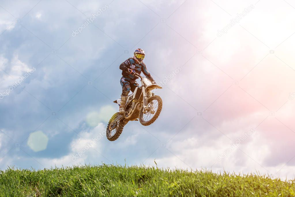 racer on a motorcycle in flight, jumps and takes off on a springboard against the sky.