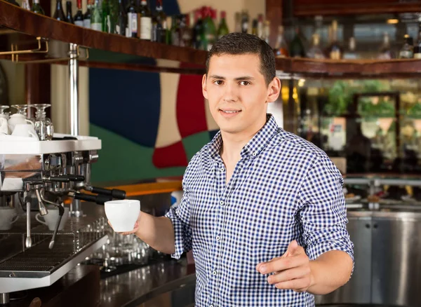 Handsome úsměvem barista držící šálek kávy a ukazující fi — Stock fotografie