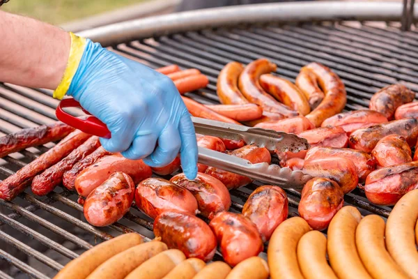 Cierre de manos asando salchichas en la barbacoa en el cálido día de verano — Foto de Stock