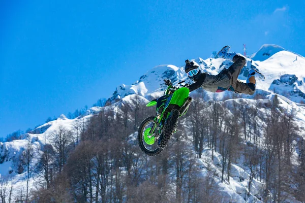 Racer on a motorcycle in flight, jumps and takes off on a springboard against the snowy mountains — Stock Photo, Image