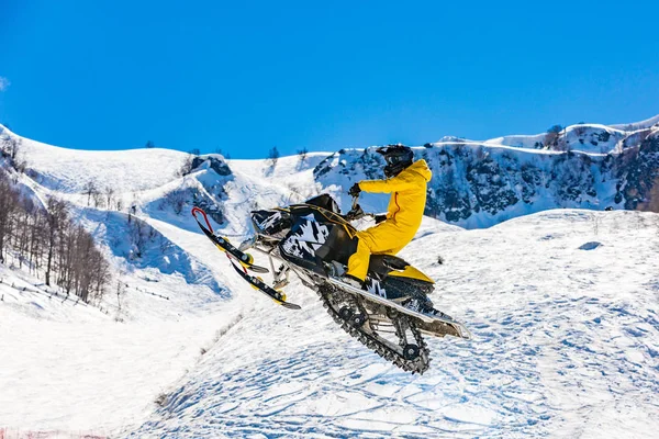 Racer na snowcat w locie, skacze i startuje na springboard przeciwko snowy góry — Zdjęcie stockowe