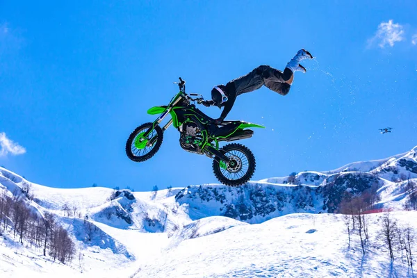 Гонщик на мотоциклі в польоті, стрибає і злітає на трампліні проти засніжених гір — стокове фото