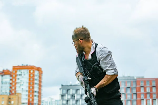 Homem vestido com um colete à prova de bala, uma camisa no sangue, persegue uma vítima com uma arma — Fotografia de Stock