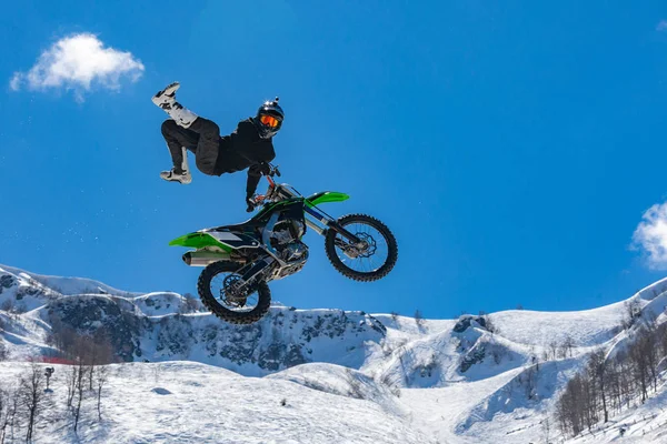 Racer na motocyklu w locie, skacze i startuje na springboard przeciwko snowy góry — Zdjęcie stockowe