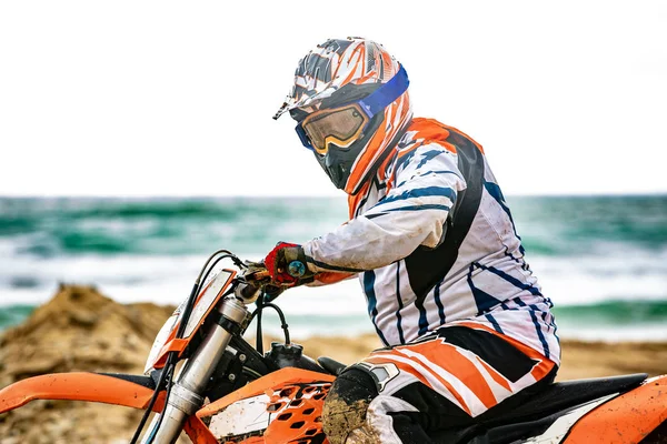 Motociclista em um terno protetor sentado em moto em frente ao mar — Fotografia de Stock