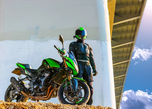 Motociclista en un casco y en un traje de protección se encuentra debajo del puente —  Fotos de Stock