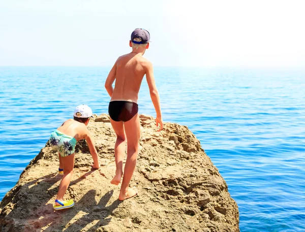 Dos chicos en bañador escalando rocas en la playa pedregosa —  Fotos de Stock