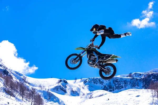 Corredor en una motocicleta en vuelo, salta y despega en un trampolín contra las montañas nevadas —  Fotos de Stock