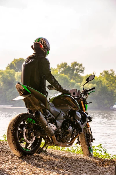 Man bär motorcykelhjälm och enhetlig sitter på cykel utomhus, vackra natursköna landskapet i bakgrunden i dagtid miljö. — Stockfoto