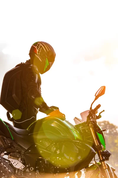 Hombre con casco de motocicleta y uniforme de seguridad sentado en bicicleta al aire libre, hermoso paisaje escénico en el fondo en el entorno diurno . —  Fotos de Stock