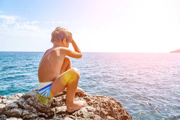 Niño en las piedras de la playa. en el fondo del agua de mar clara —  Fotos de Stock