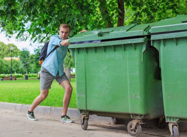 Man pushing a green garbage cans in the park clipart