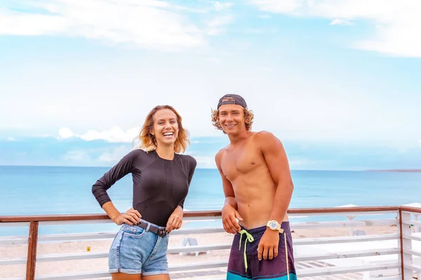 Χαμογελώντας νεαρό ζευγάρι ενεργό surfers χαλαρώνοντας στην παραλία μετά τον αθλητισμό — Φωτογραφία Αρχείου