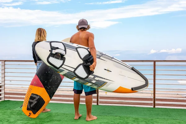 Χαμογελώντας νεαρό ζευγάρι ενεργό surfers χαλαρώνοντας στην παραλία μετά τον αθλητισμό με σανίδα του σερφ. Υγιεινού τρόπου ζωής. Ακραία σπορ — Φωτογραφία Αρχείου