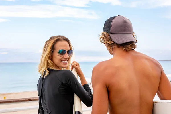 Giovani surfisti sorridenti di coppia attiva che si rilassano sulla spiaggia dopo lo sport — Foto Stock