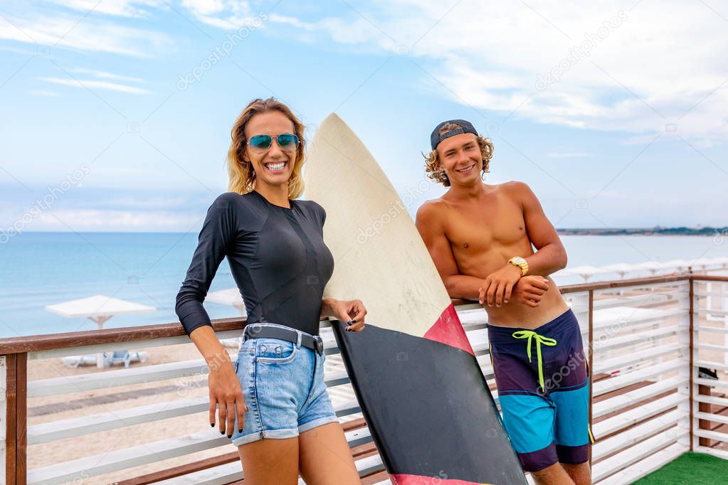 Smiling young active couple surfers relaxing on the beach after sport with Surfboard. Healthy Lifestyle. Extreme Water Sports