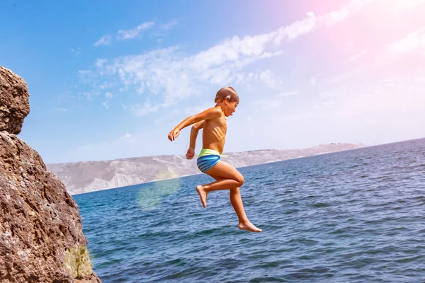 Хлопчик стрибає зі скелі в море в спекотний літній день. Відпочинок на пляжі. Концепція активного туризму та відпочинку — стокове фото