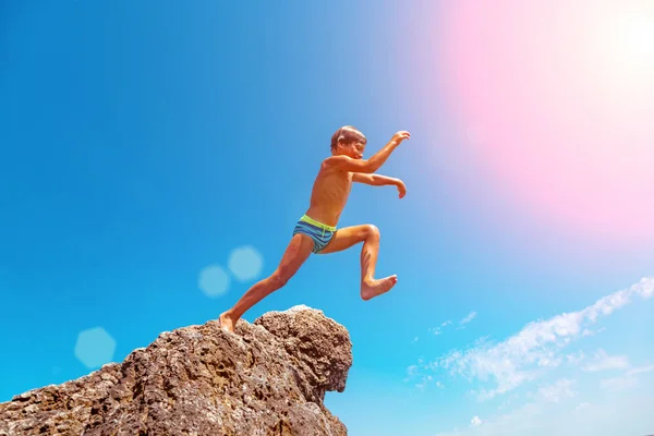 Un niño está saltando desde el acantilado hacia el mar en un caluroso día de verano. Vacaciones en la playa. El concepto de turismo activo y recreación — Foto de Stock