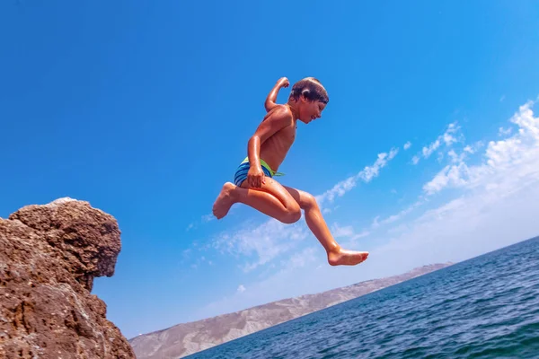 Chłopiec skacze z klifu do morza na upalne dni. Wakacje na plaży. Pojęcie turystyki aktywnej i rekreacji — Zdjęcie stockowe