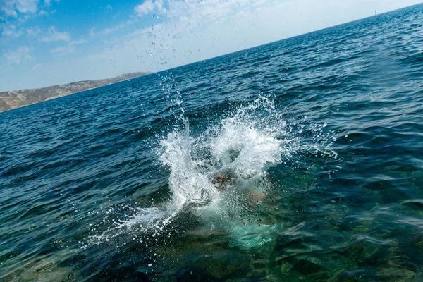 En pojke hoppar från klippan i havet med stora vattenstänk på en varm sommardag. Semester på stranden. Begreppet aktiv turism och rekreation — Stockfoto