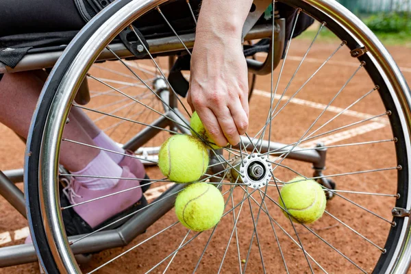 Gehandicapte jonge vrouw in rolstoel tennissen op de tennisbaan. Close-up van een hand neemt een tennisbal vast in een wiel — Stockfoto