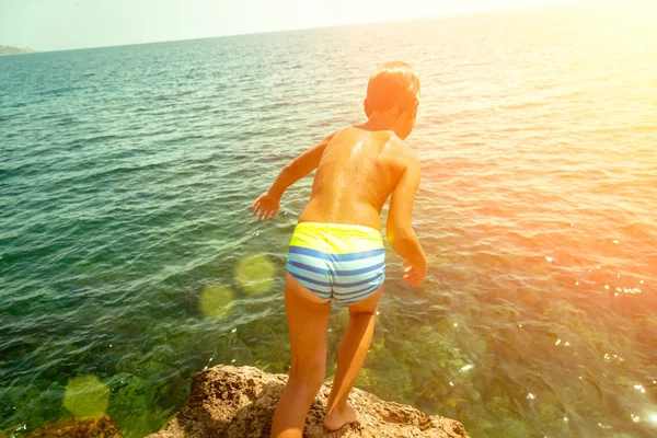 Un niño está saltando desde el acantilado hacia el mar en un caluroso día de verano. Vacaciones en la playa. El concepto de turismo activo y recreación —  Fotos de Stock