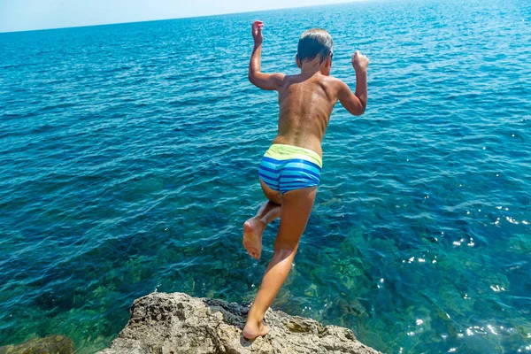 Een jongen is springen uit de rots in de zee op een hete zomerdag. Vakantie op het strand. Het concept van actief toerisme en recreatie — Stockfoto