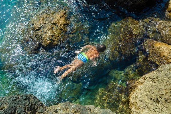 En pojke hoppar från klippan i havet en varm sommardag. Semester på stranden. Begreppet aktiv turism och rekreation — Stockfoto