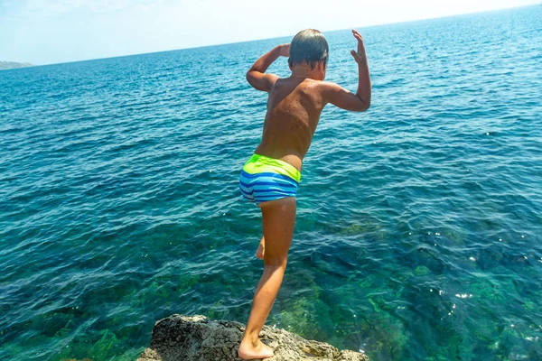 Un ragazzo sta saltando dalla scogliera in mare in una calda giornata estiva. Vacanze sulla spiaggia. Il concetto di turismo attivo e ricreazione — Foto Stock