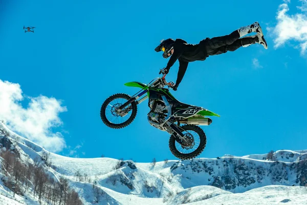 Piloto em uma motocicleta em voo, salta e decola em um trampolim contra as montanhas nevadas — Fotografia de Stock