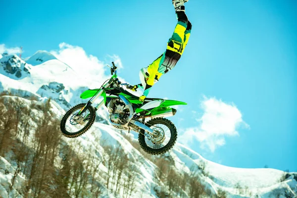 Гонщик на мотоцикле в полете, прыгает и взлетает на трамплине против снежных гор — стоковое фото