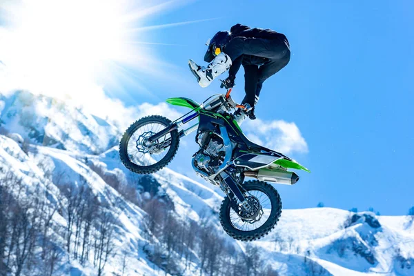 Racer op een motorfiets tijdens de vlucht, springt en neemt af op een springplank tegen de besneeuwde bergen — Stockfoto