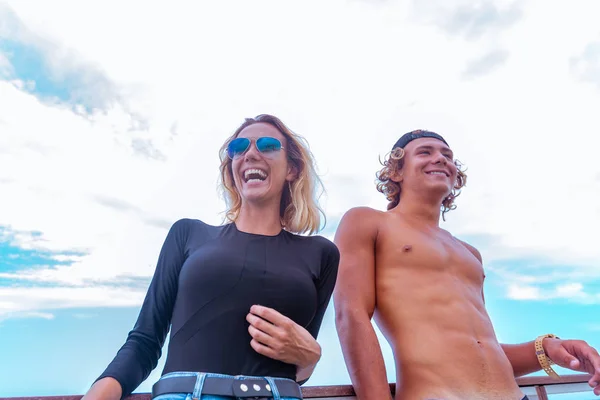 Χαμογελώντας νεαρό ζευγάρι ενεργό surfers έχοντας διασκέδαση στην παραλία μετά τον αθλητισμό. Όμορφη Θαλασσογραφία στο φόντο — Φωτογραφία Αρχείου