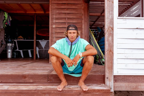 The surfer sits on the terrace on the beach looking out into the camera. — Stock Photo, Image